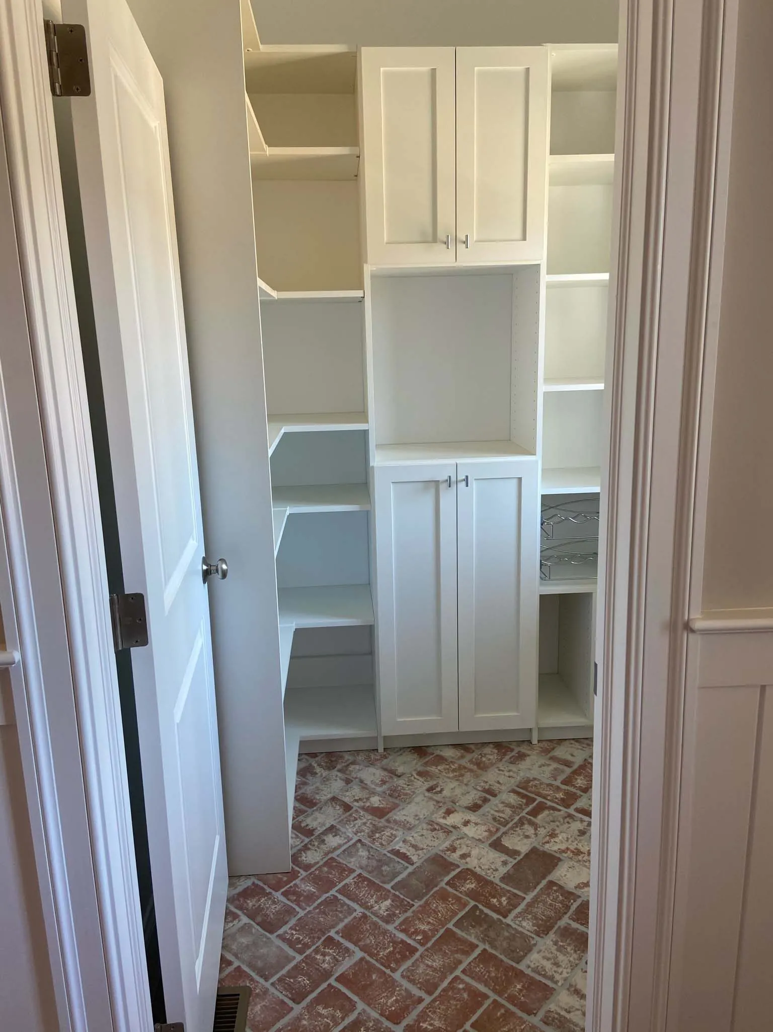 White closet with shelving and drawers behind an open door, on a brick floor