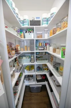 White walk-in pantry with wraparound shelving stocked with food