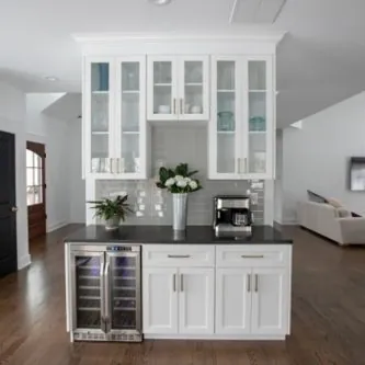 White built-in bar with glass-front cabinets, a wine fridge and a dark counter