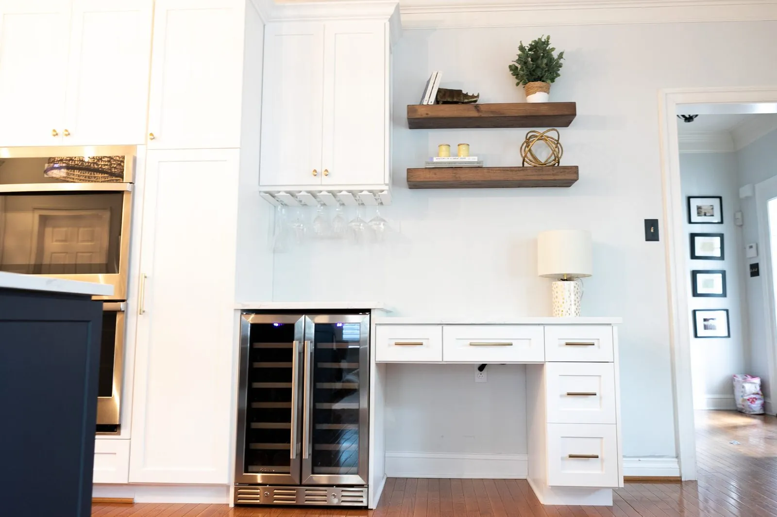 White built-in desk with floating shelves beside a wine fridge