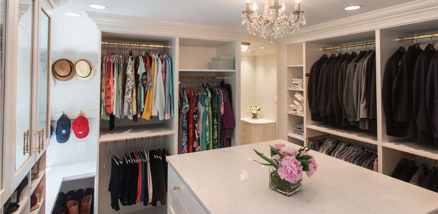 White walk-in closet with an island under a chandelier, hanging and shelving