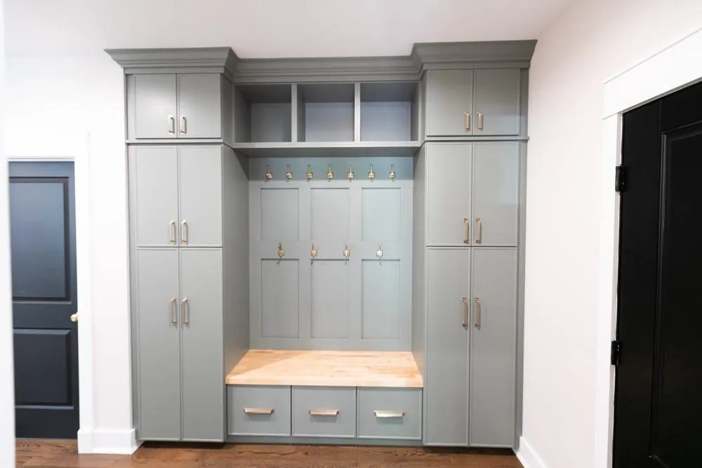Gray mudroom lockers with hooks, a wood-top bench and tall cabinets