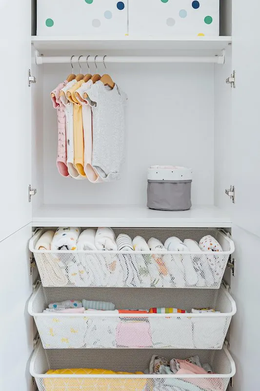 White closet with hanging children's clothes above pull-out baskets