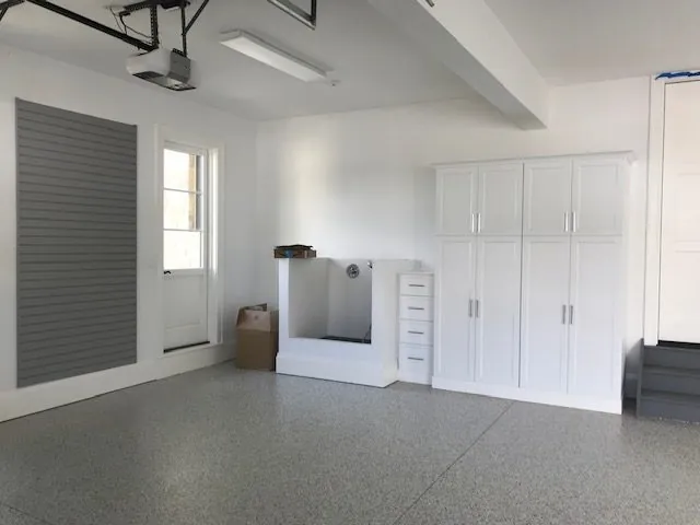 Garage with gray slatwall, a dog wash station and tall white cabinets