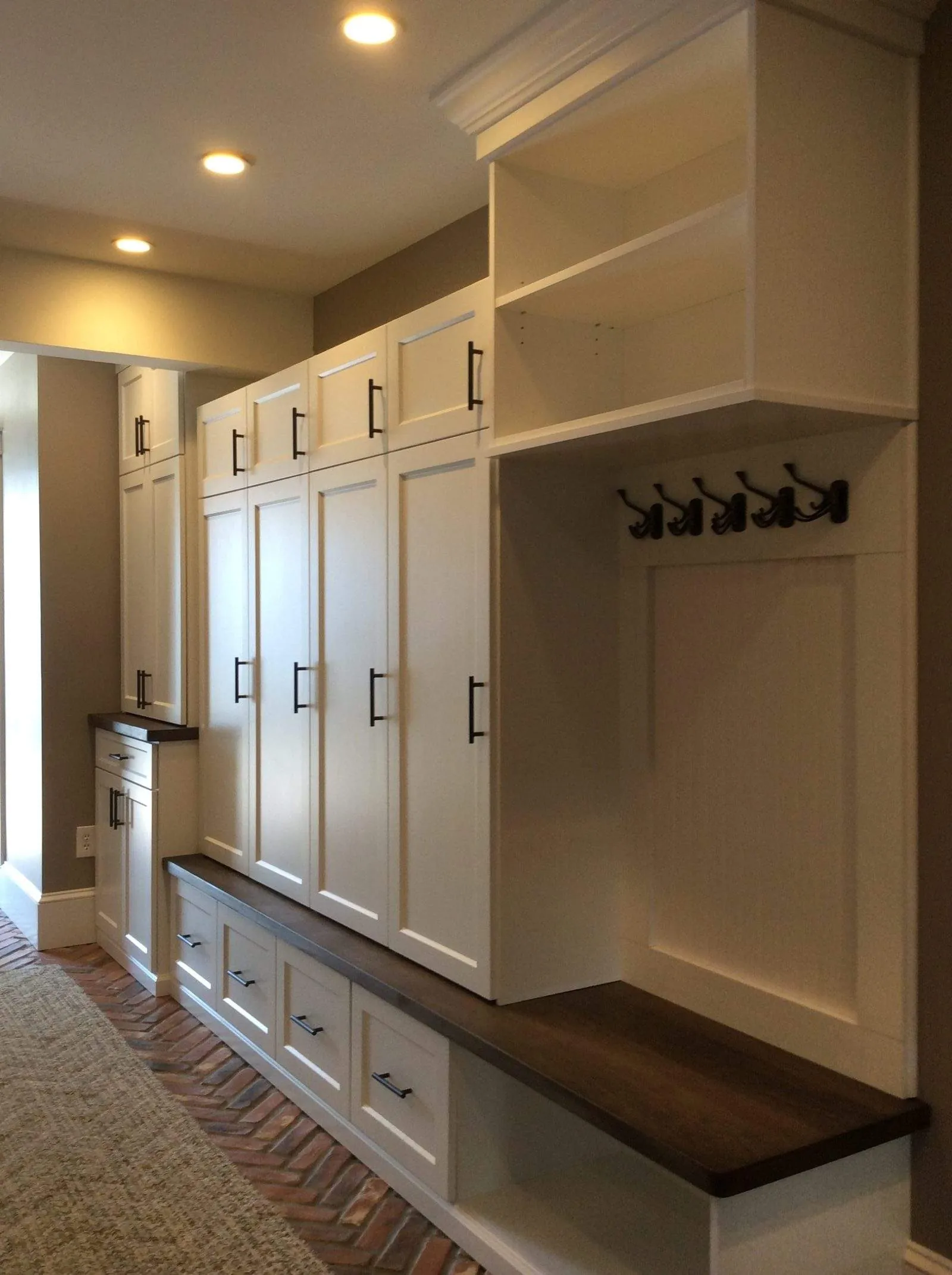White mudroom with tall cabinets, hooks and a wood bench