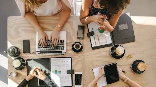 People working at a table with laptops, tablets and coffee