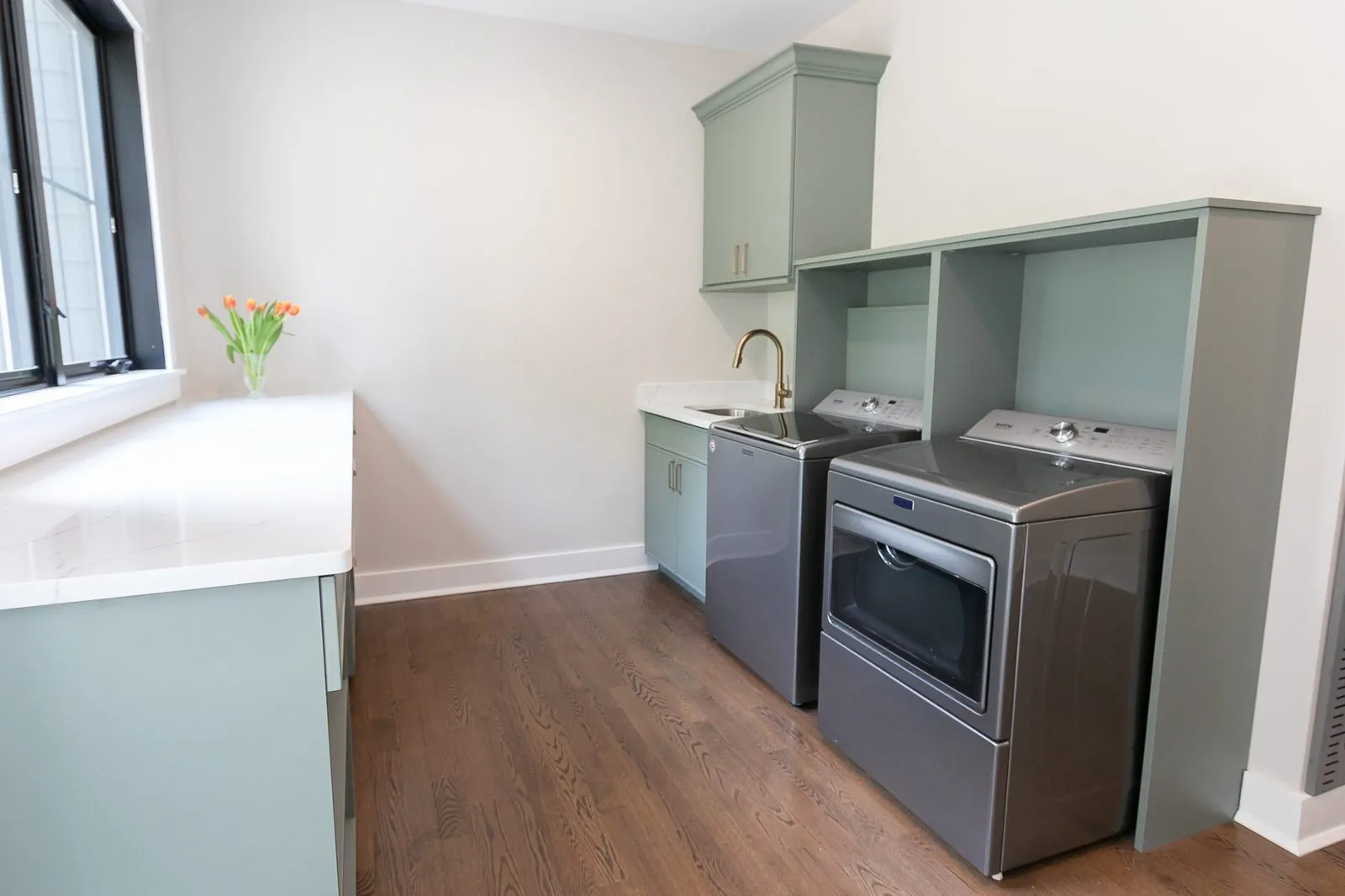 Sage green laundry cabinets around a gray washer and dryer, beside a white counter