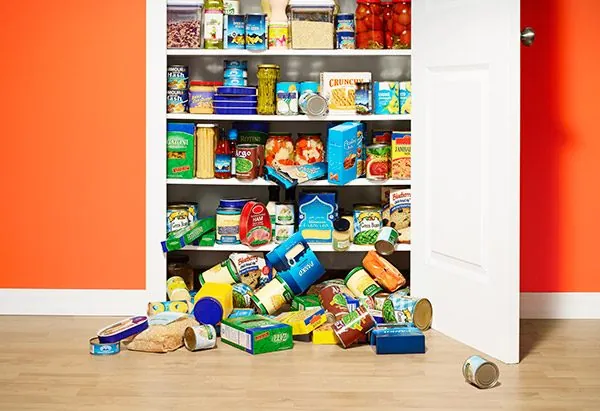 Overflowing pantry shelves with cans and boxes spilling onto the floor