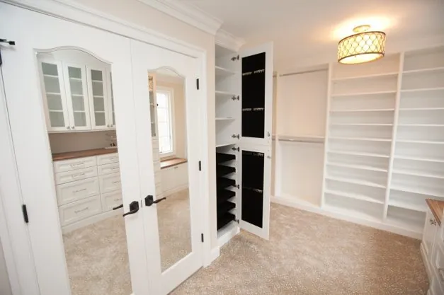 Walk-in closet with shelving and drawers behind French doors with a mirror