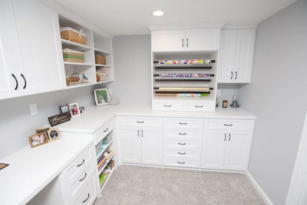 White L-shaped room with a desk, upper cabinets, drawers and a wrapping paper rack