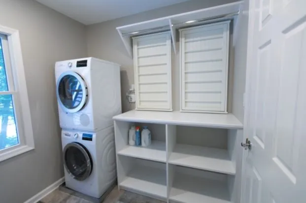 Stacked washer and dryer beside white cabinets with louvered doors