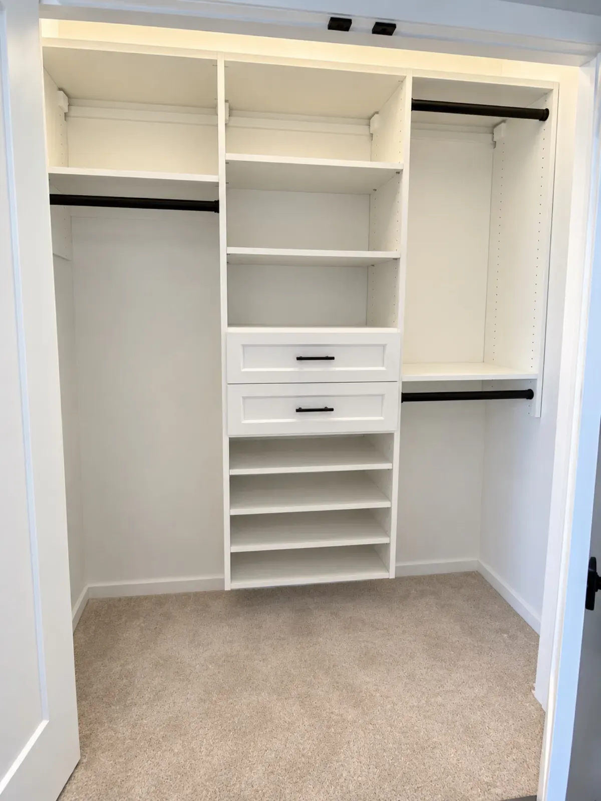 Reach-in closet with black rods, a center shelf tower and two drawers