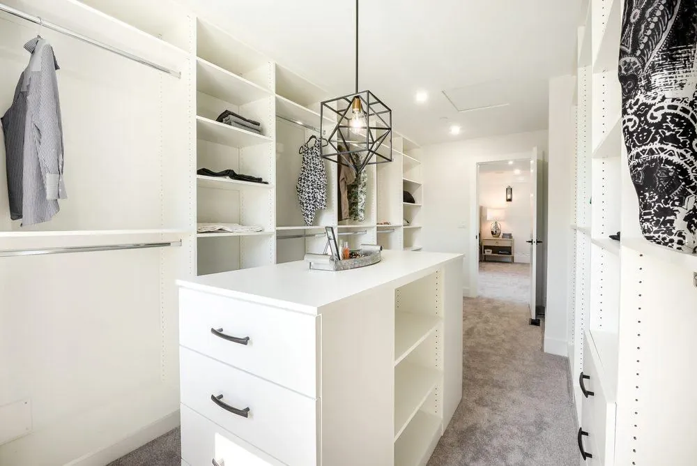 White closet with shelving, hanging clothes and a center island under a pendant light