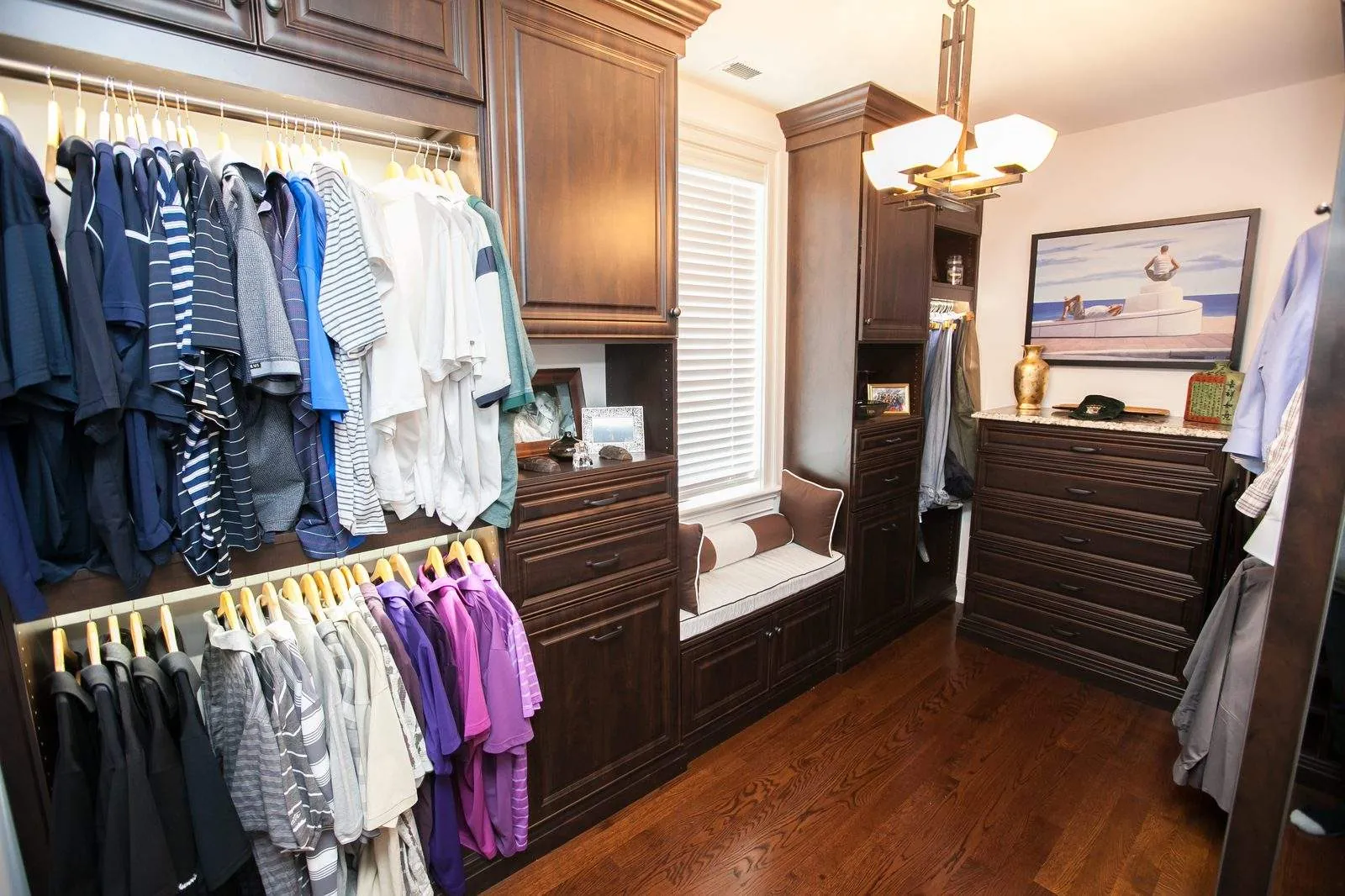 Dark wood walk-in closet with hanging, drawers and a window seat