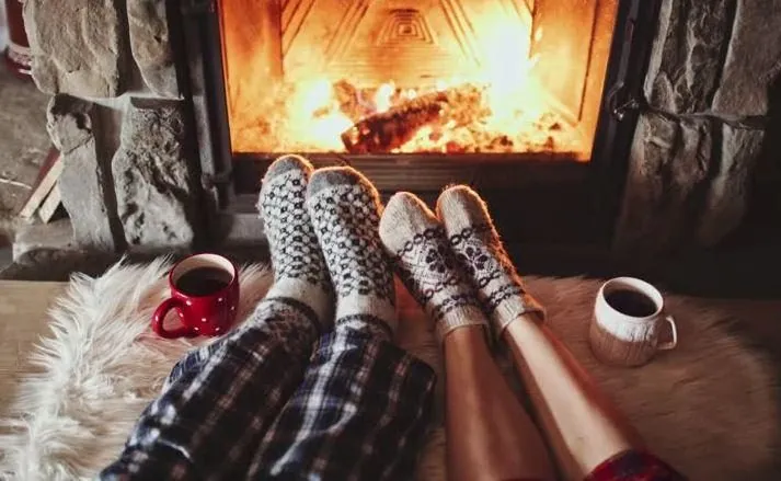 Feet in cozy socks by a fireplace with mugs