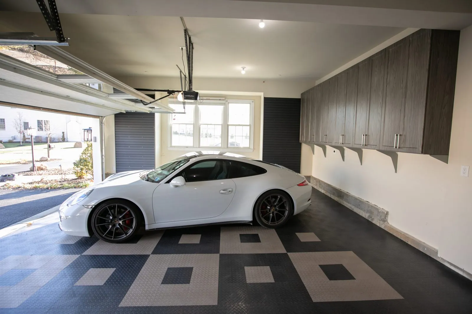 Garage with gray wall cabinets beside a white sports car on a patterned floor