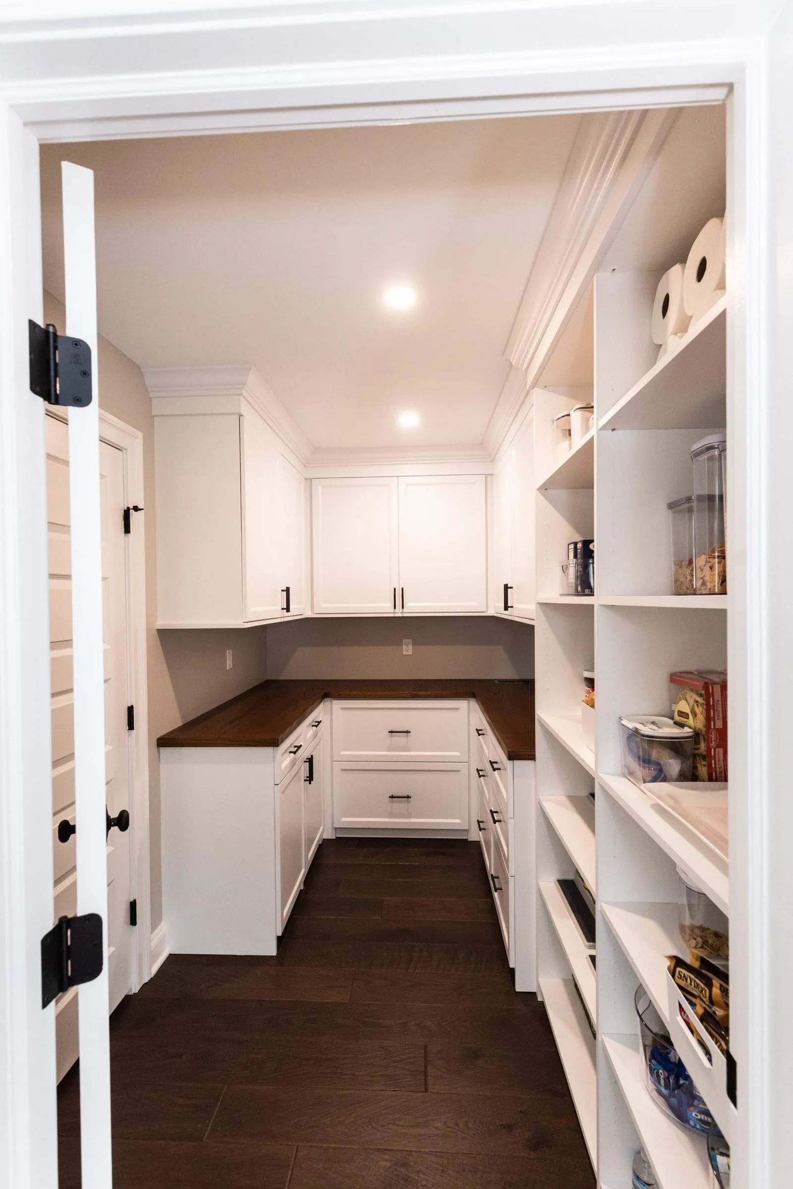 White pantry with shelving and a wood counter, seen through the door