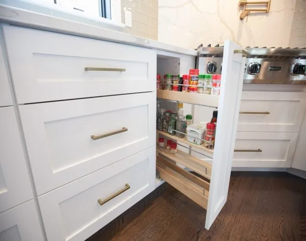 Pull-out pantry cabinet with stocked shelves beside white drawers