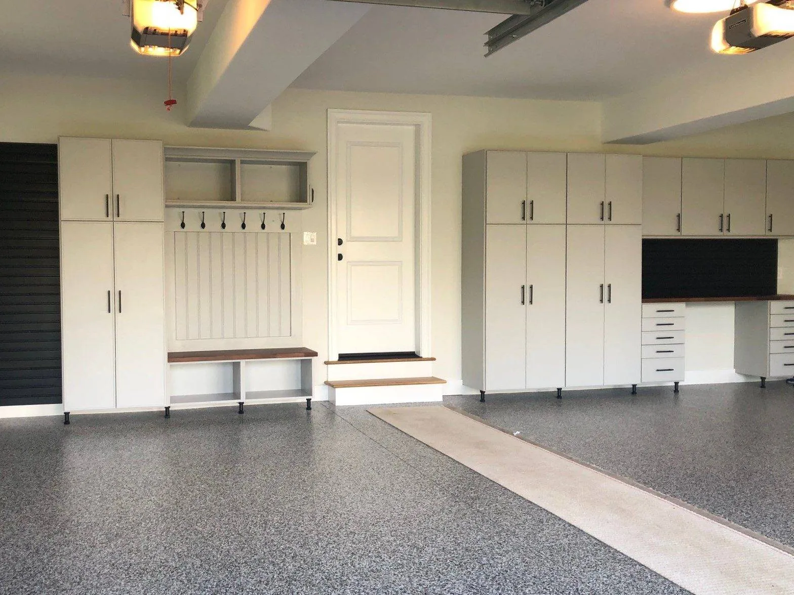 Garage with tall white cabinets, a bench with hooks and a workbench on an epoxy floor