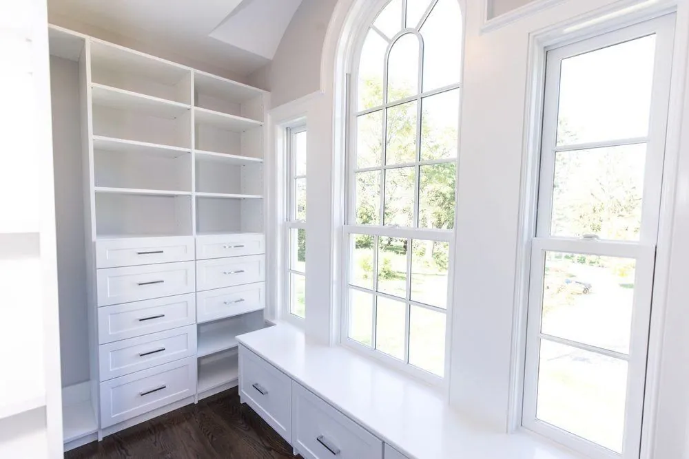White closet with a drawer stack and a window bench beside arched windows