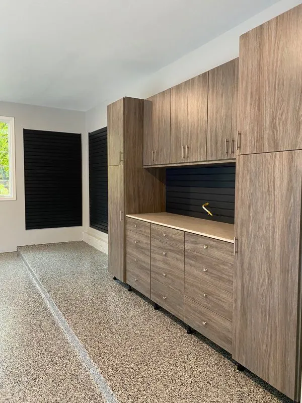 Wood-grain garage cabinets beside black slatwall on an epoxy floor