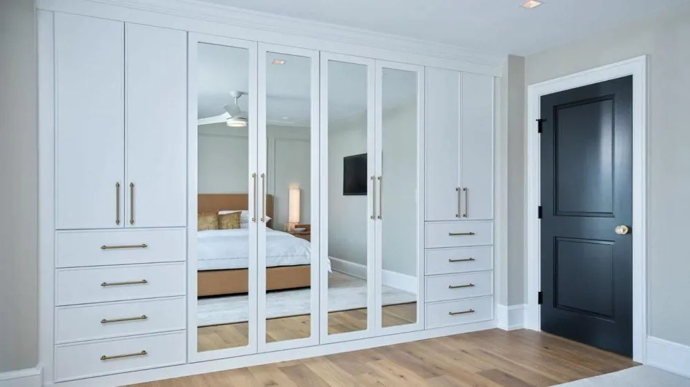 White wardrobe with mirrored doors and gold handles in a bedroom
