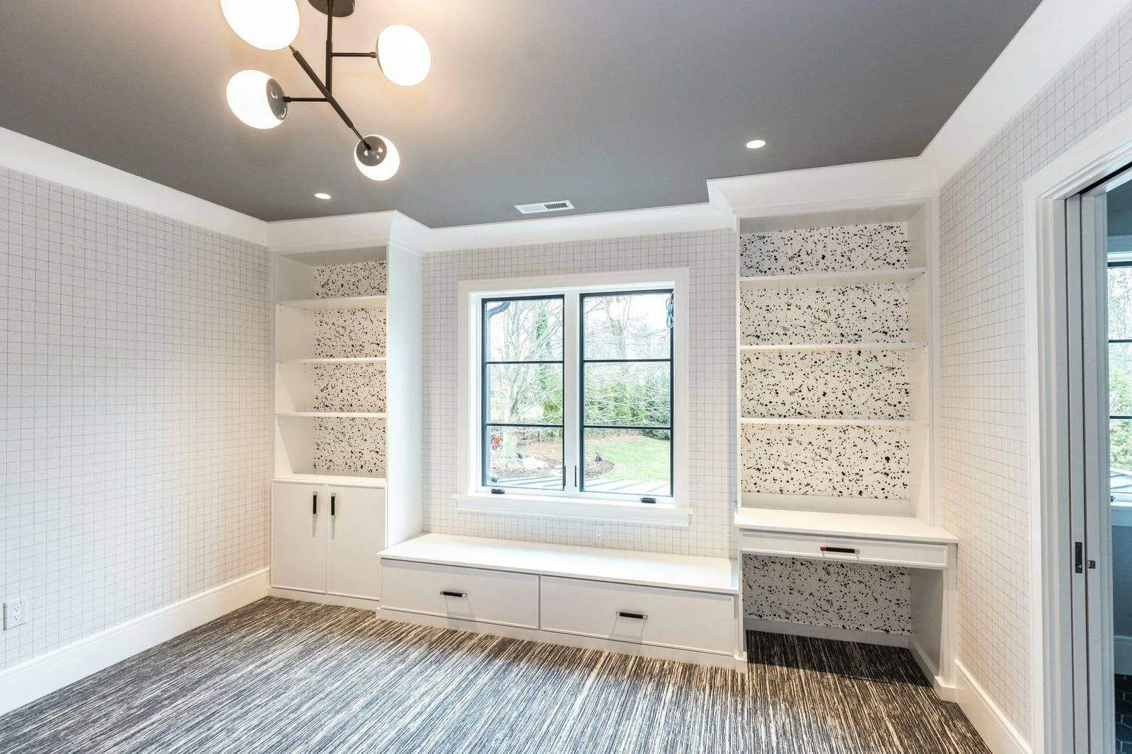 Window seat with drawers between patterned-back bookcases under a modern light fixture