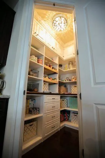 Narrow pantry with lit shelves seen through an open door