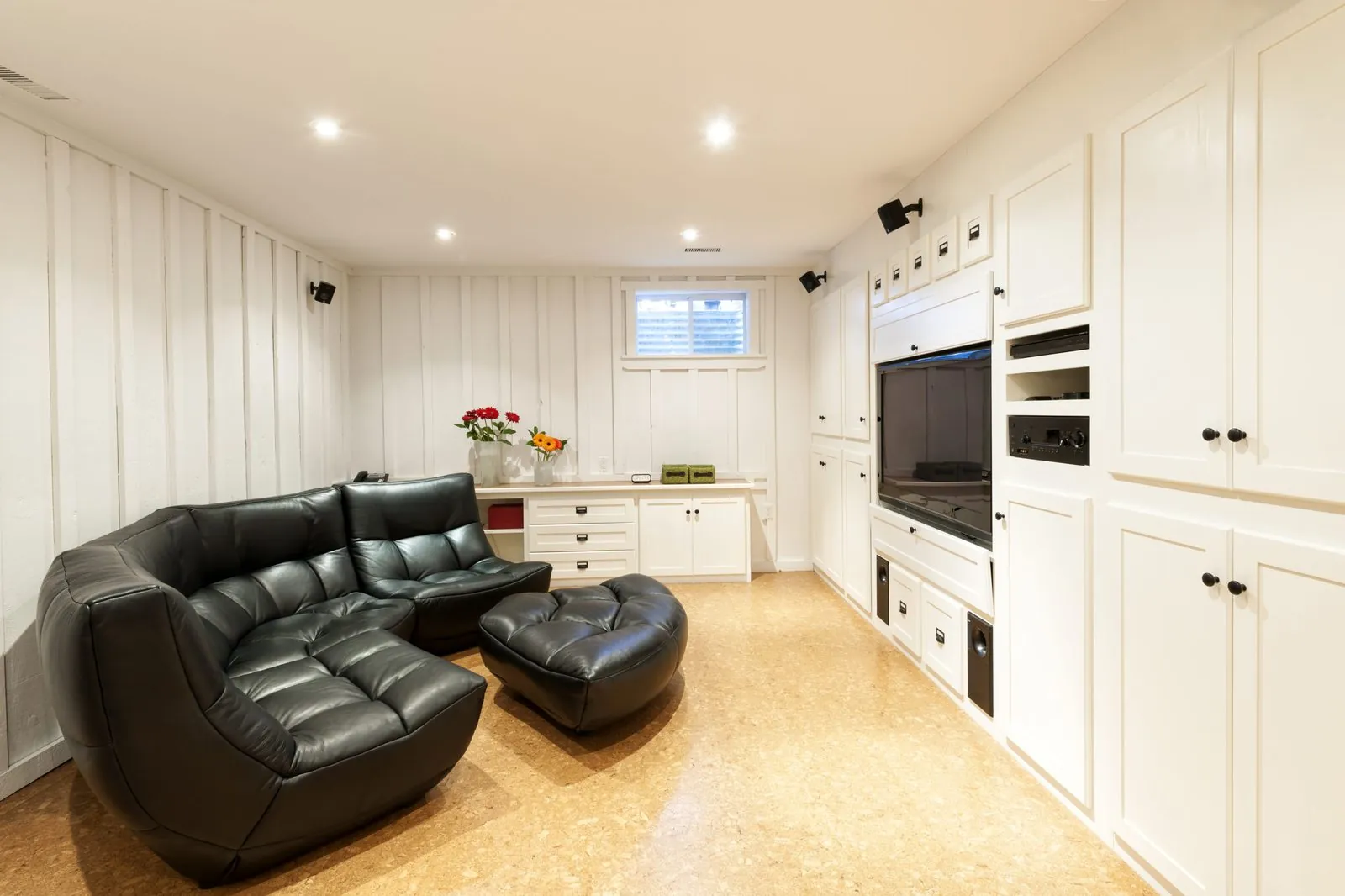 Basement media room with white built-in cabinets, a TV and a black leather sofa