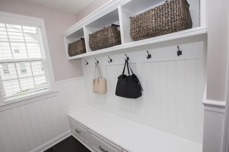 White mudroom bench with hooks and upper cubbies with baskets