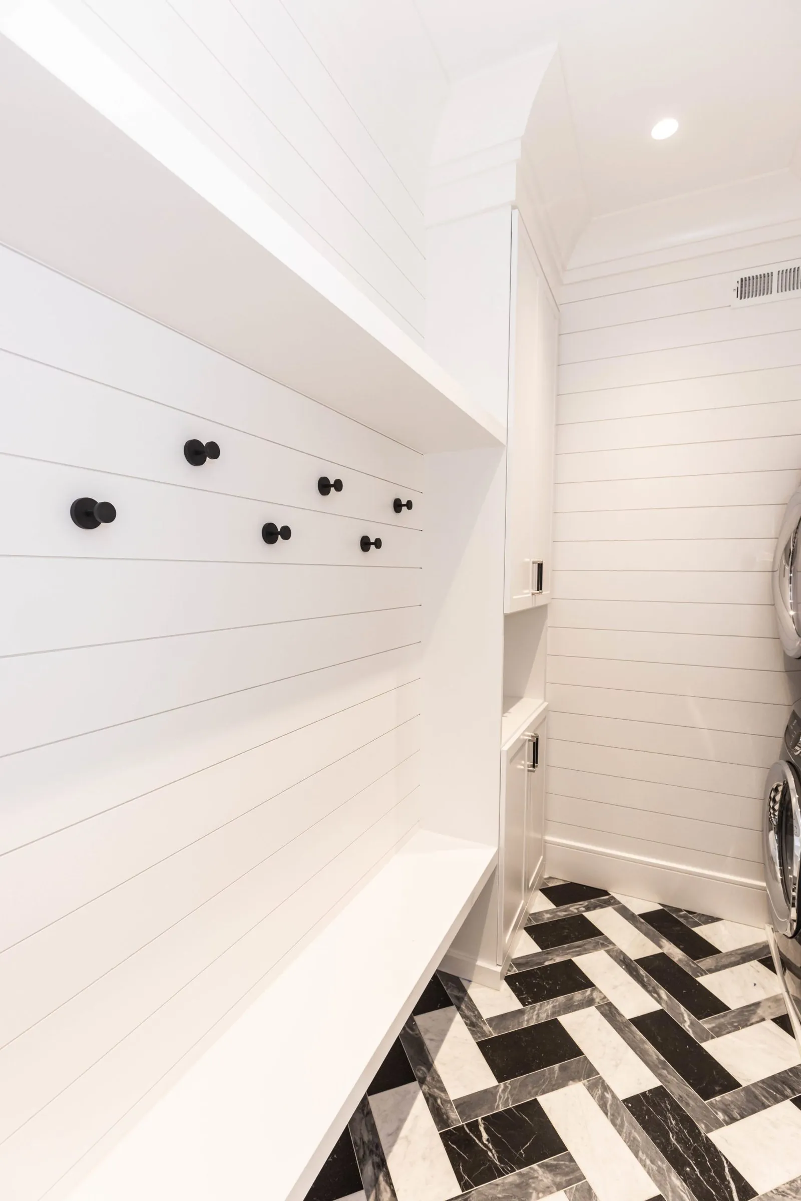 White mudroom wall with black hooks over a checkered floor