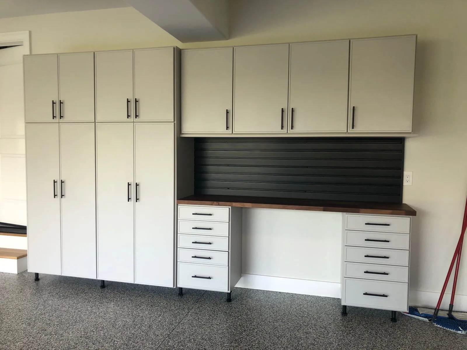 Tall white garage cabinets and drawers with black slatwall over a workbench