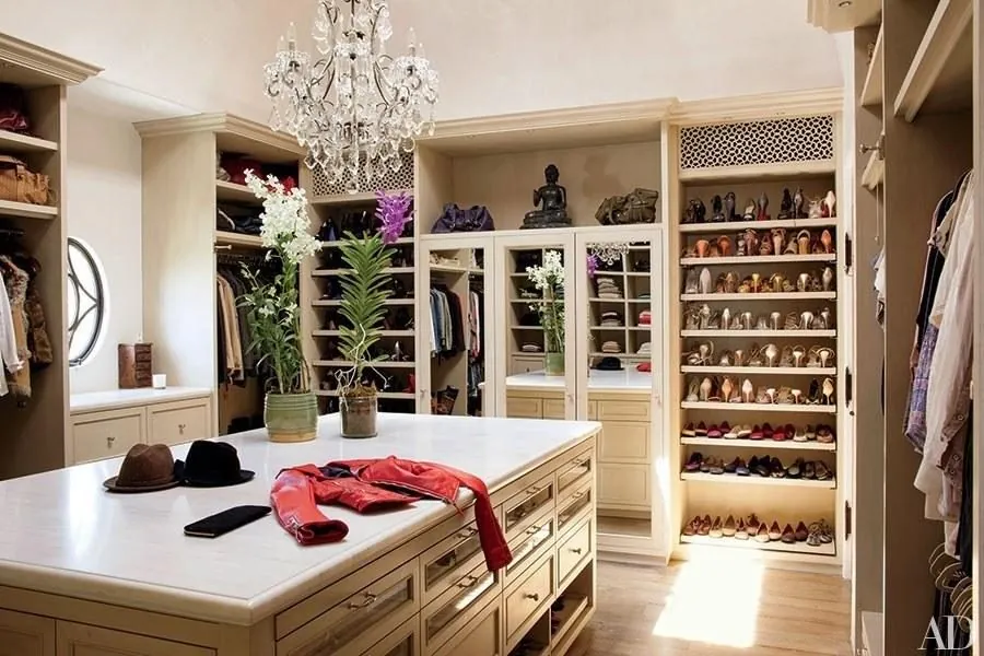 Walk-in closet with a center island under a chandelier and lit shoe shelving