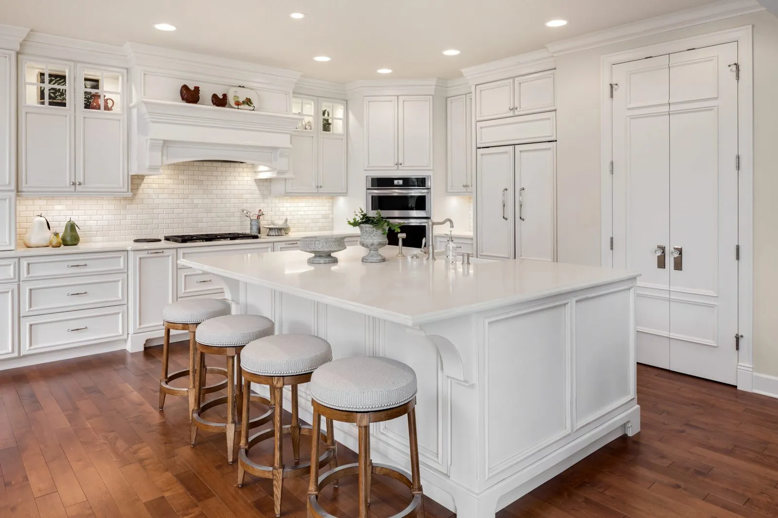 White kitchen with a large island, stools and tall cabinets