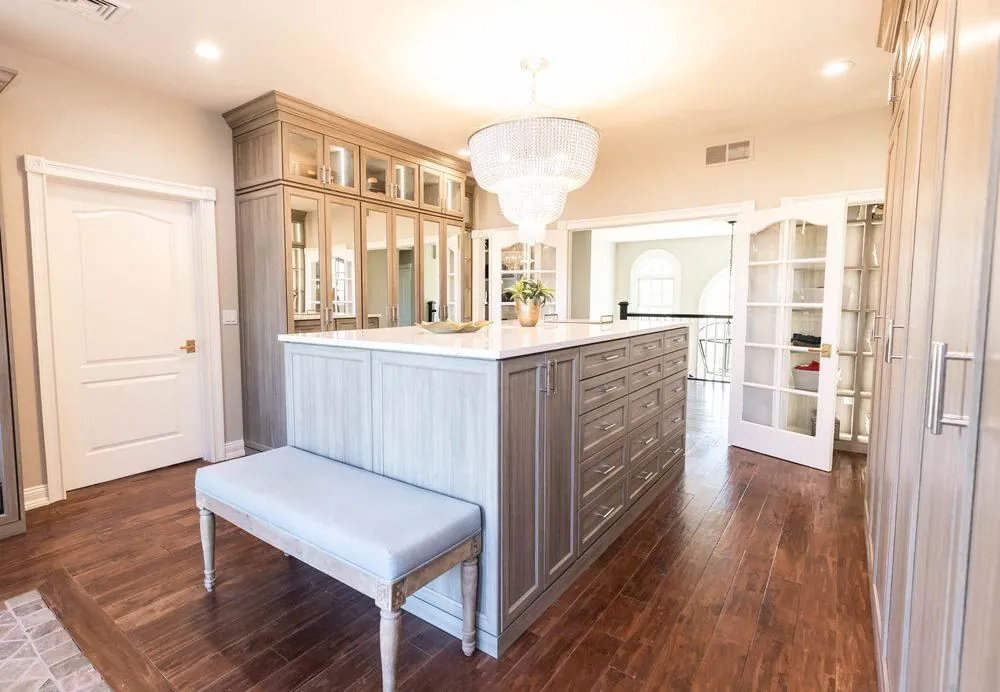 Walk-in closet with a wood-grain island, an upholstered bench and cabinets under a chandelier