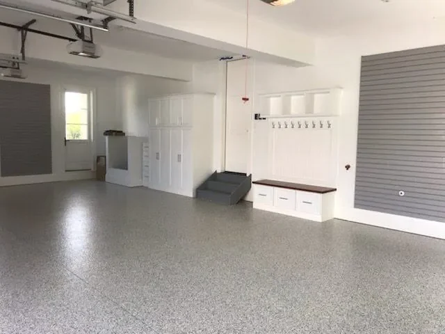 Garage with tall white cabinets, a bench with hooks and gray slatwall on an epoxy floor