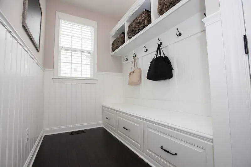 White mudroom bench with hooks and cubbies with baskets beside a window