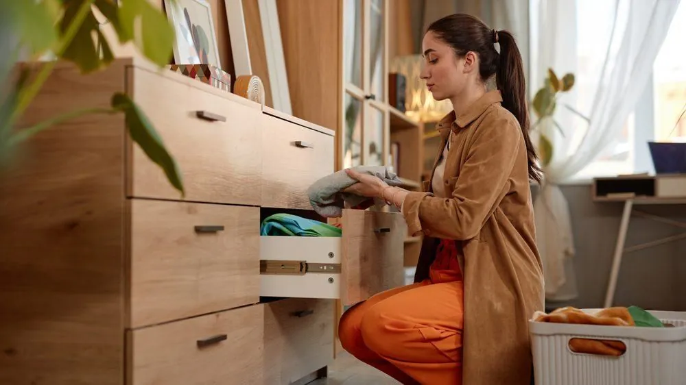 Woman kneeling to put clothes into an open wood drawer