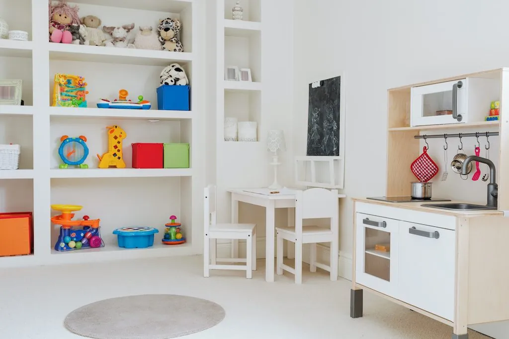 White playroom shelving with toys, a play kitchen and a small table