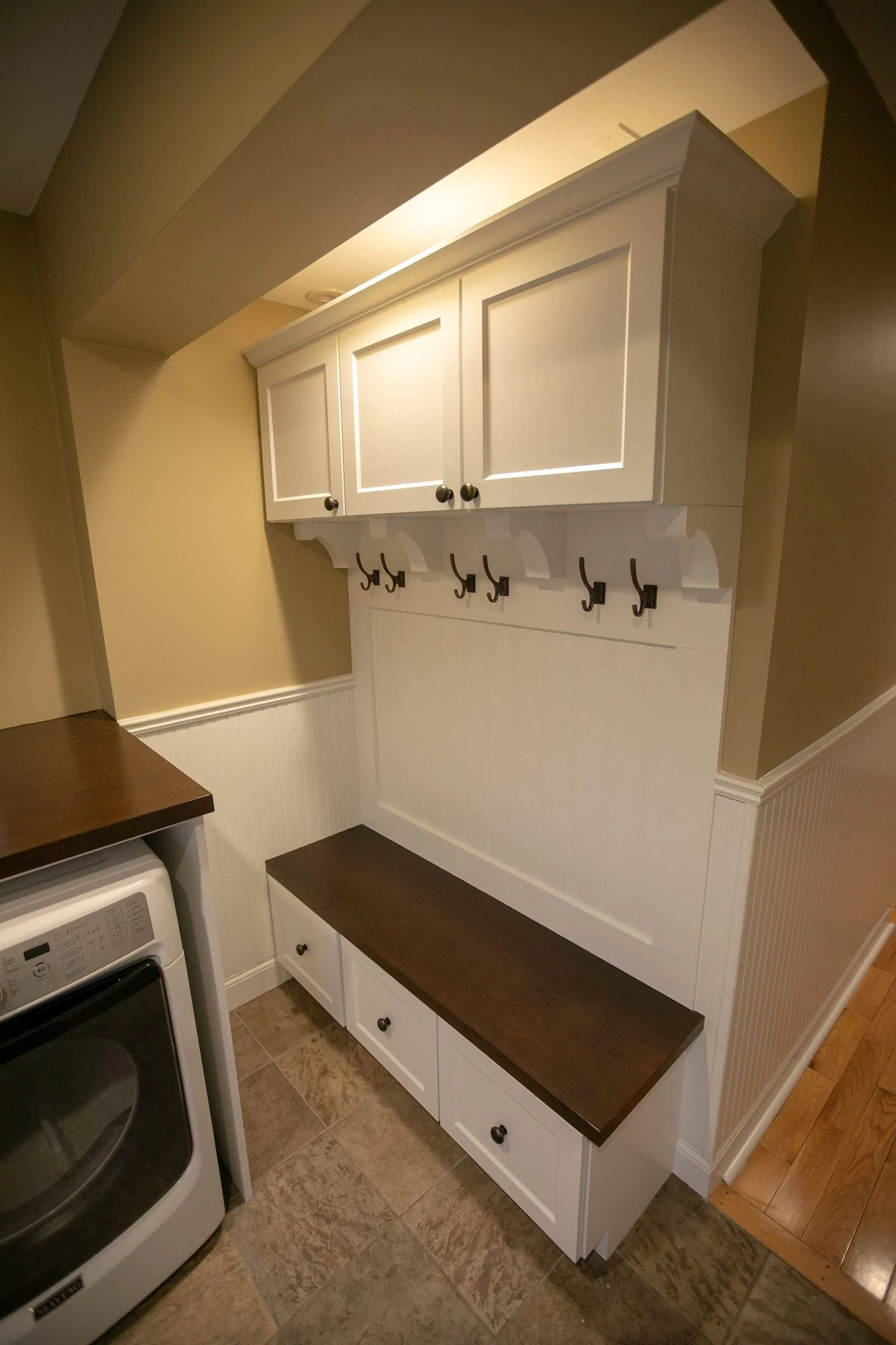 White mudroom cubby with hooks and a bench beside a washer