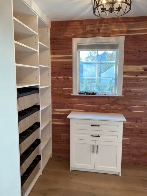 White shelving and a small cabinet beside a red brick wall and window