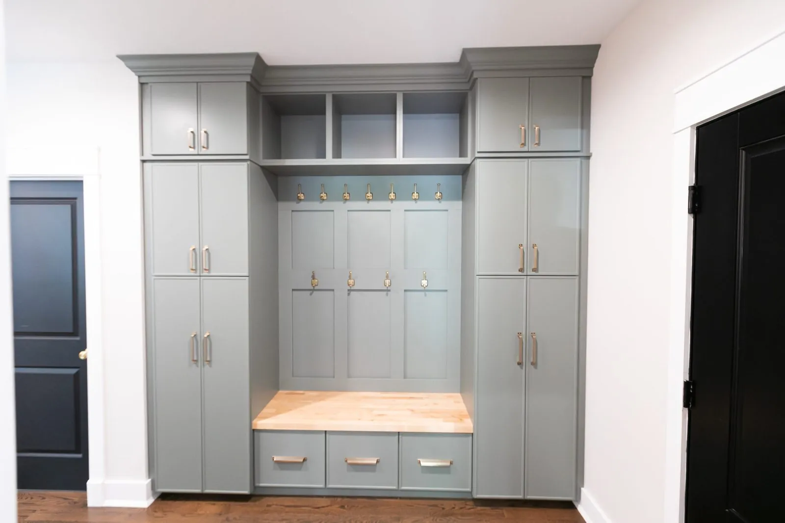 Gray mudroom lockers with hooks, a wood-top bench and tall cabinets