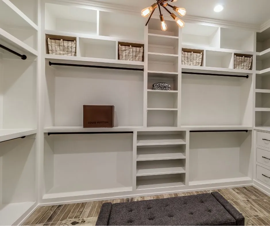 White walk-in closet with open cubbies, baskets and shelving under a pendant light