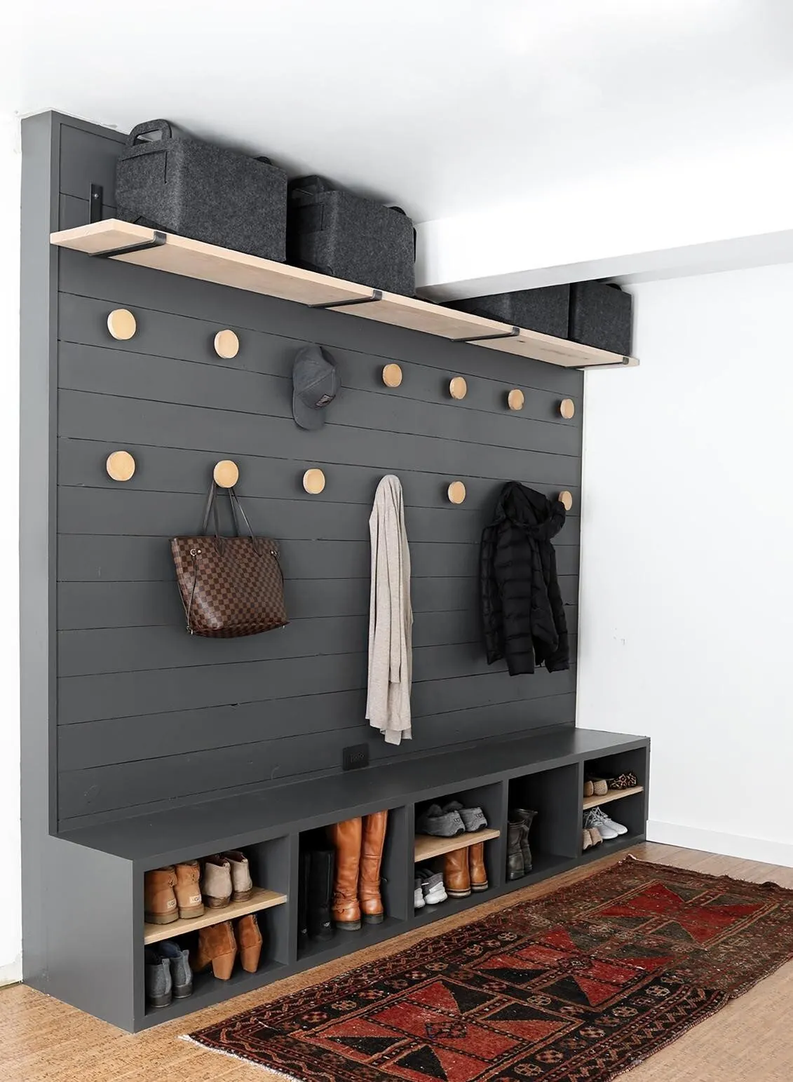 Black pegboard mudroom wall with hooks, a coat and a bench with cubbies over a rug