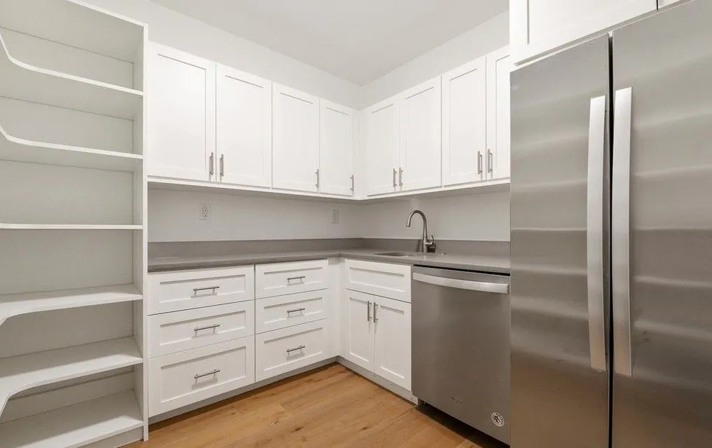 White kitchen with corner pantry shelving, shaker cabinets and a stainless refrigerator