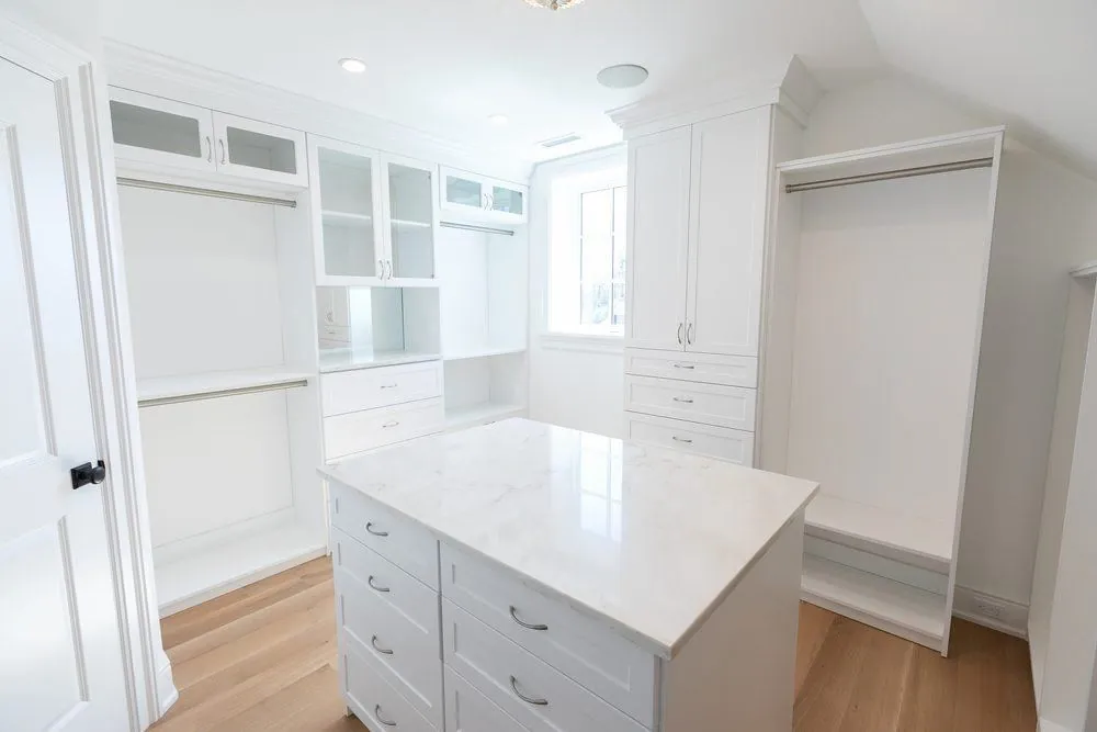White walk-in closet with an island, glass-front cabinets and hanging