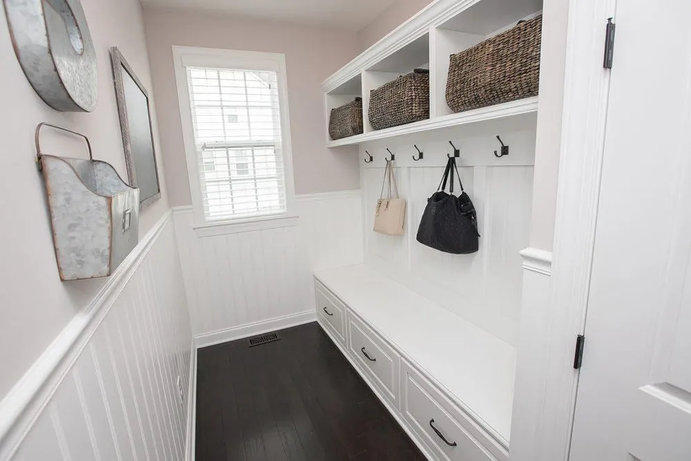 White mudroom bench with hooks and upper cubbies with baskets against a beadboard wall
