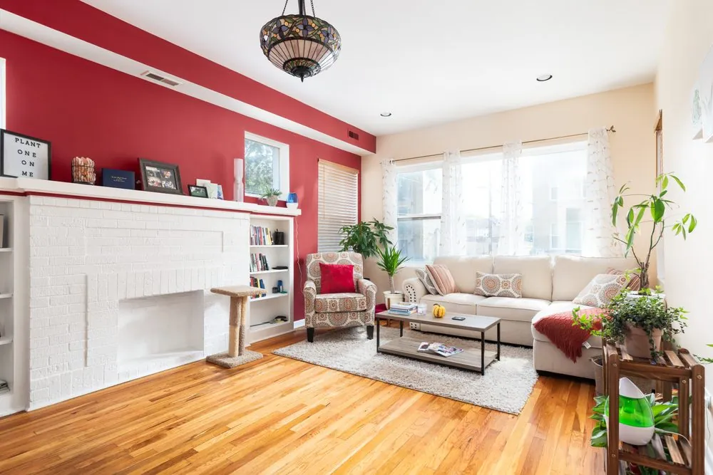 Living room with a red accent wall, a white fireplace and built-in shelving