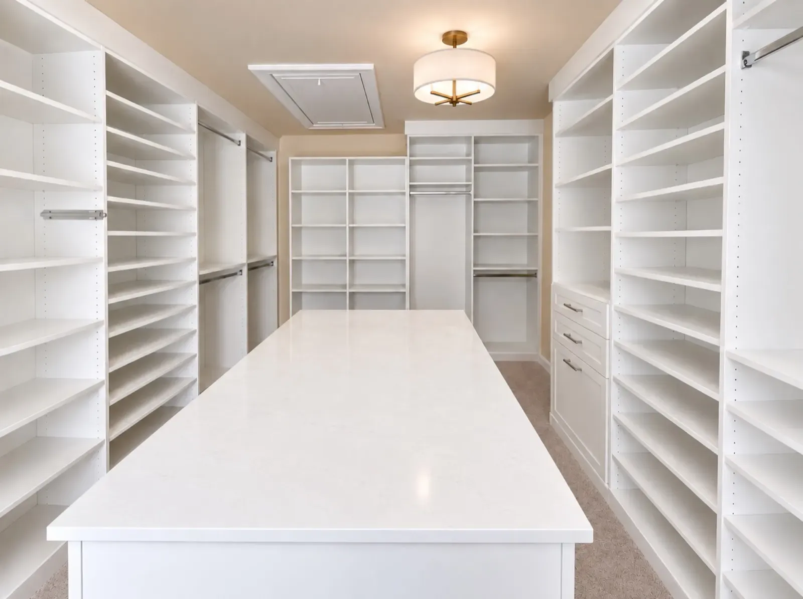 White walk-in closet with a long white island between full shelving walls