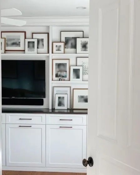 White built-in media cabinet with a TV and framed photos above